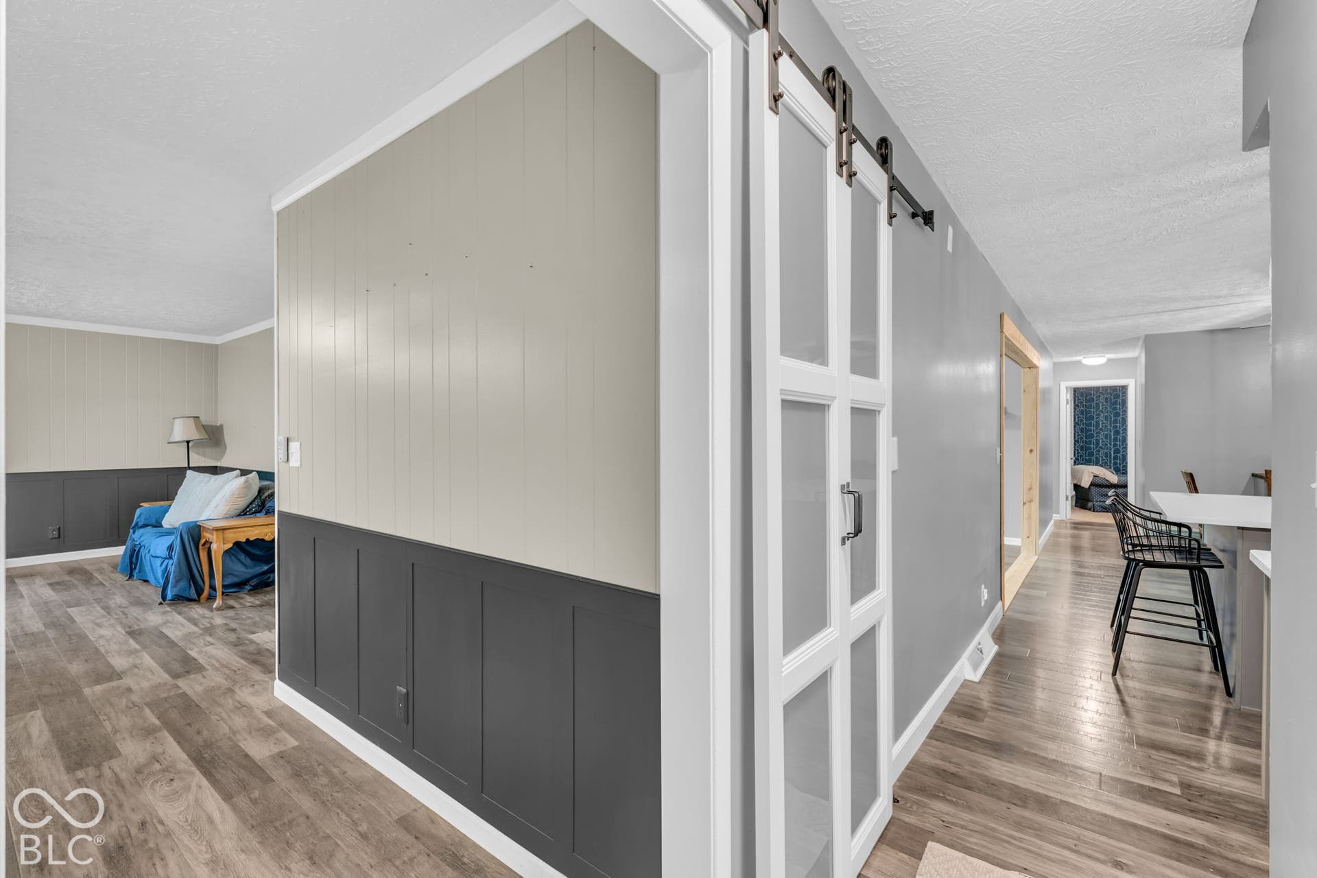 Wood-finish flooring throughout, two-tone wainscoting, and a modern barn door with frosted glass panels