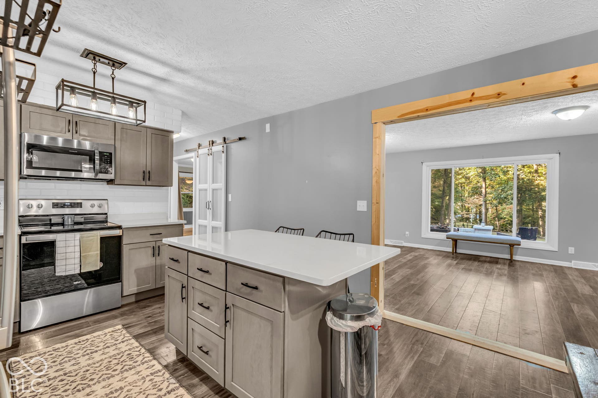Kitchen featuring a central island with white countertop, stainless steel appliances, wood-finish flooring, and a barn door entry