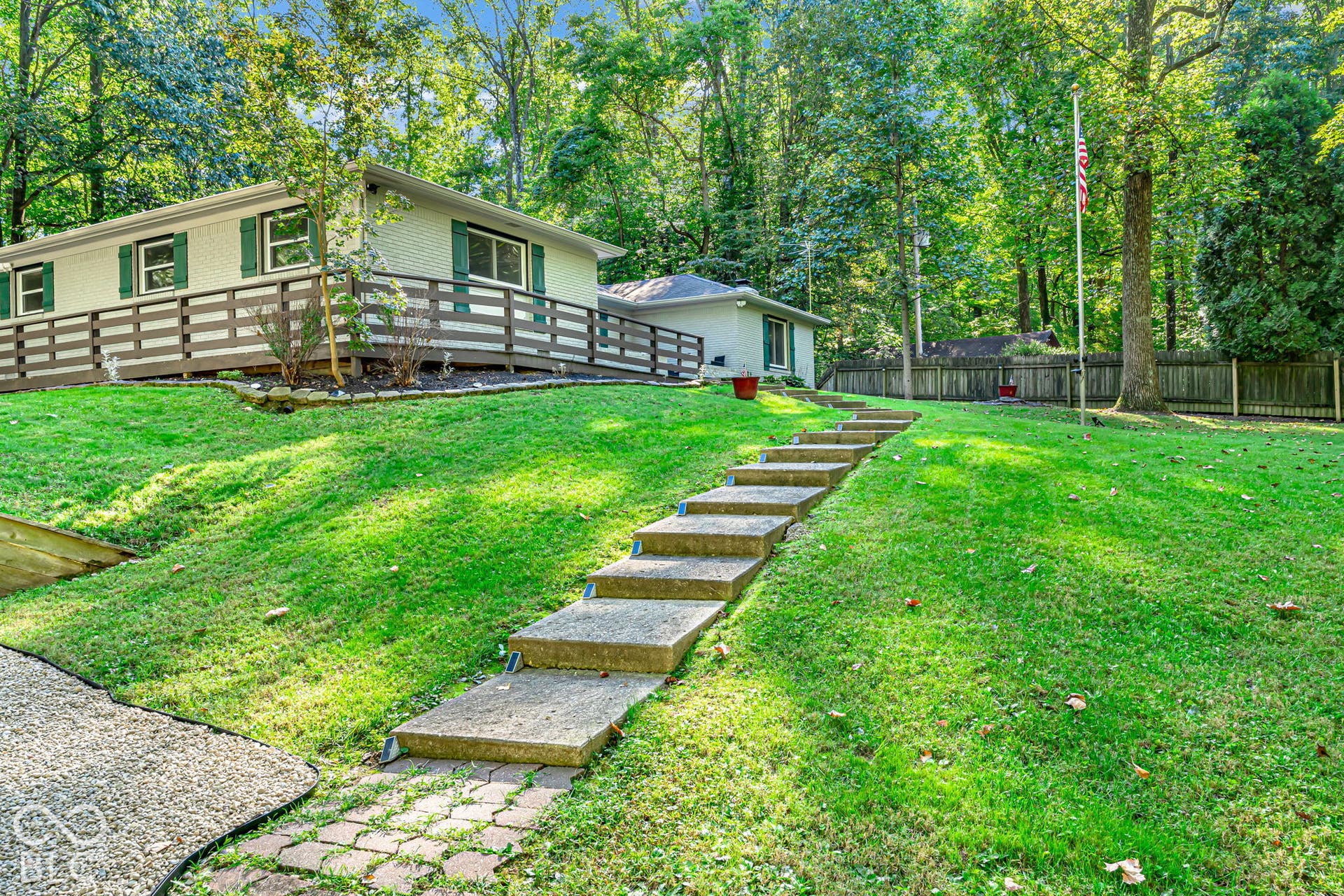 Expansive green lawn with established trees, concrete and paver pathway, and sloped landscaping