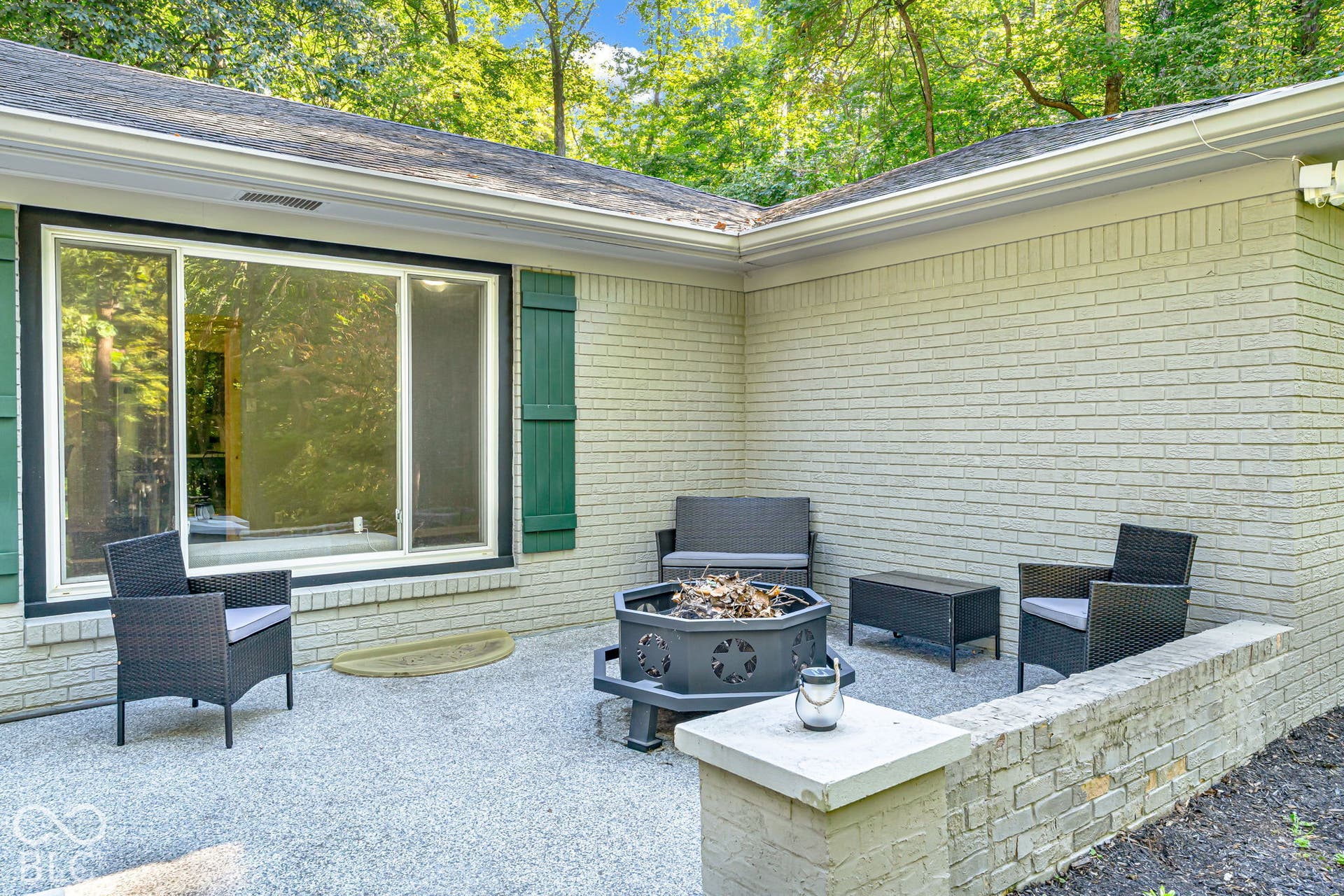 Expansive outdoor patio featuring a durable stone-finish surface, a low brick retaining wall, and a large sliding glass door