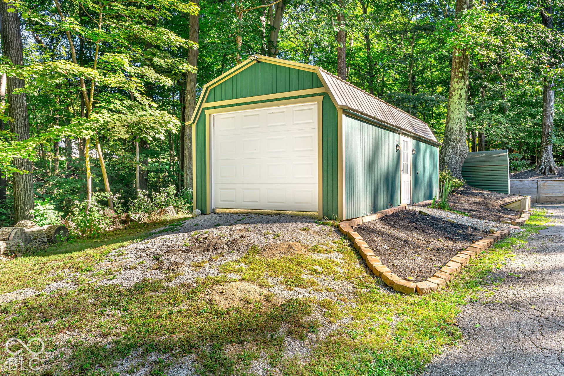 Green utility building with a white overhead door, side entry door, and metal roof