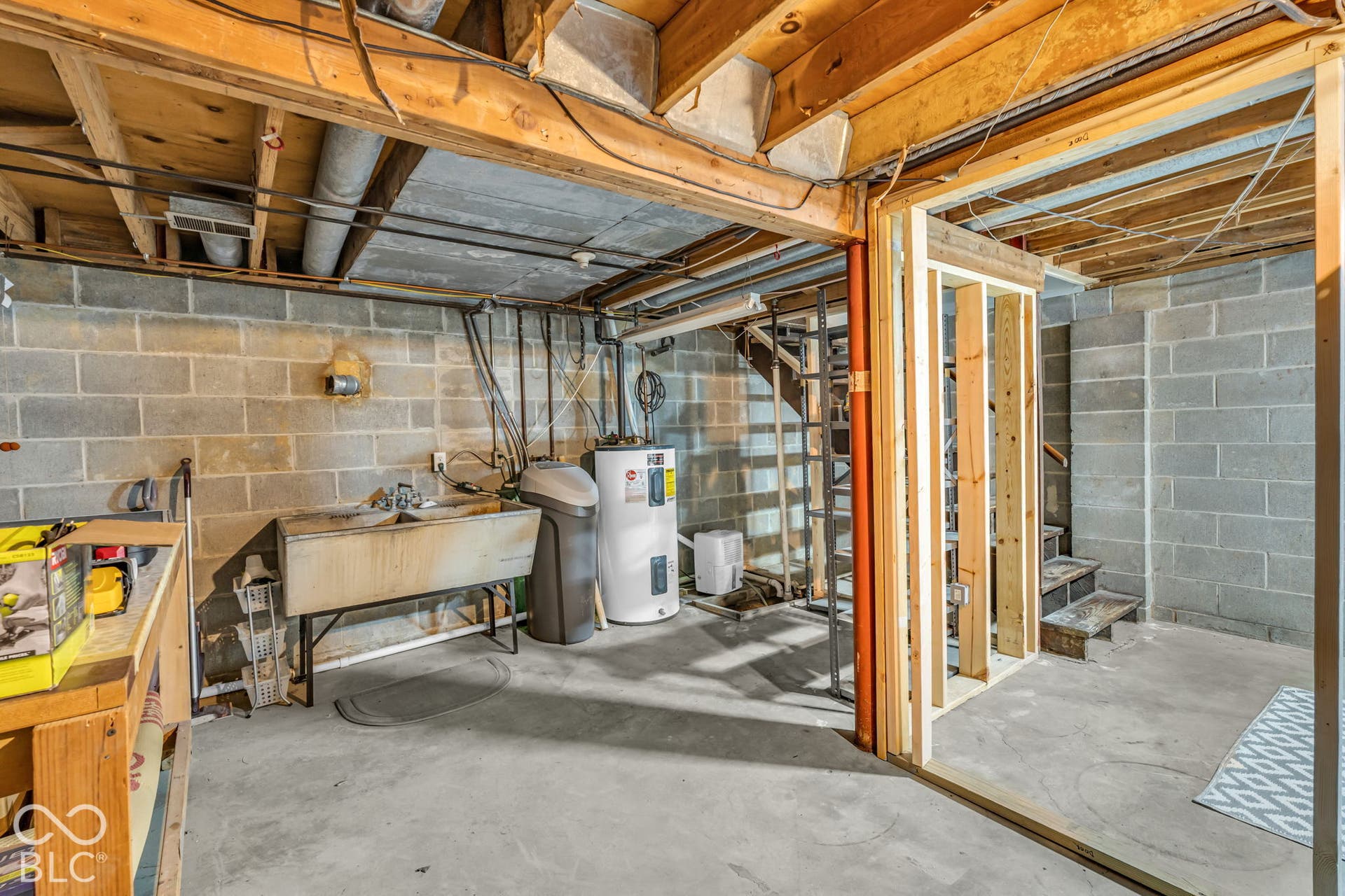 Concrete block walls, exposed wood ceiling joists, concrete flooring, utility sink, and water heater