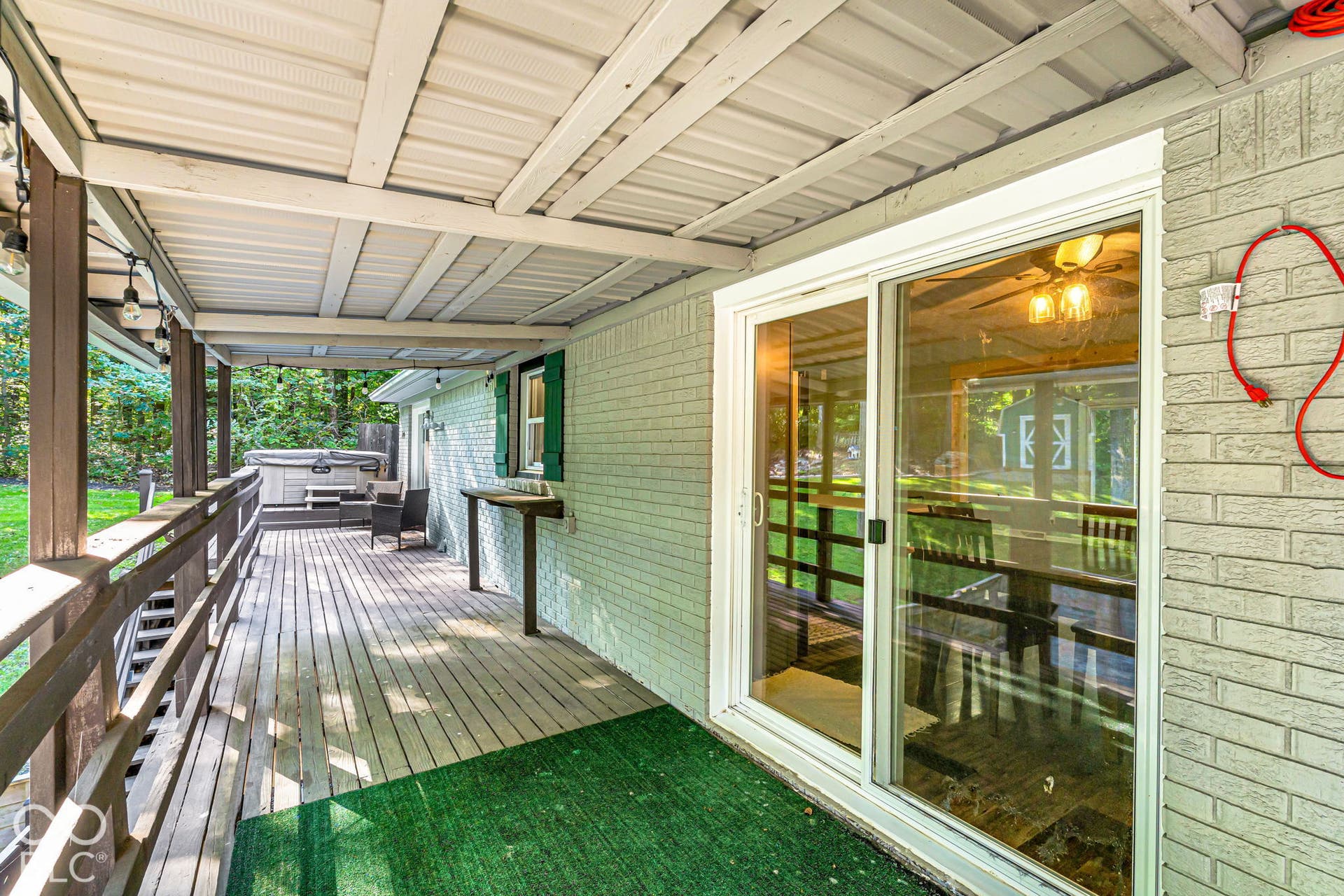Covered outdoor deck with a metal roof, wood flooring, and a built-in hot tub