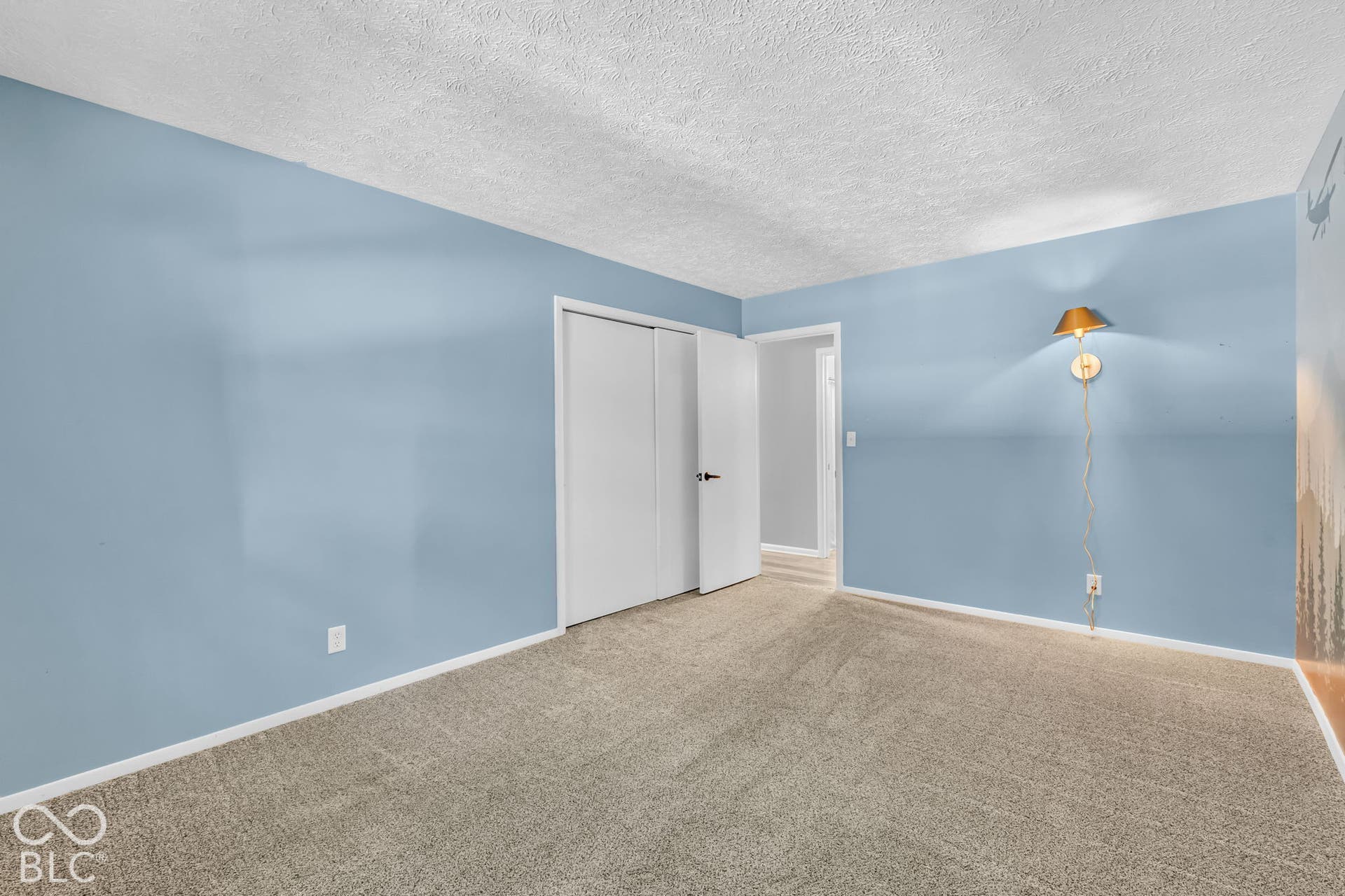 Carpeted flooring, light blue wall paint, white trim, white bi-fold closet doors, and a wall-mounted sconce