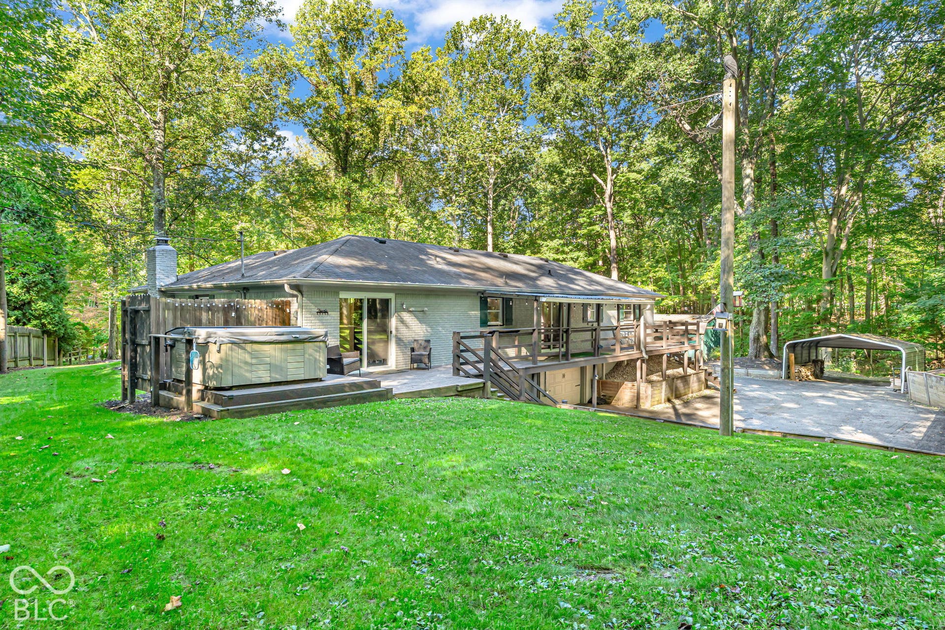 Expansive green lawn, elevated wood deck, sliding glass doors, detached carport, and mature trees