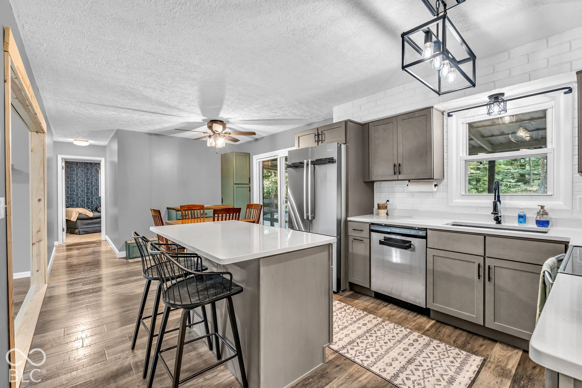 Kitchen featuring wood-finish flooring, a central island with white countertop, gray cabinetry, stainless steel appliances, and a white subway tile backsplash