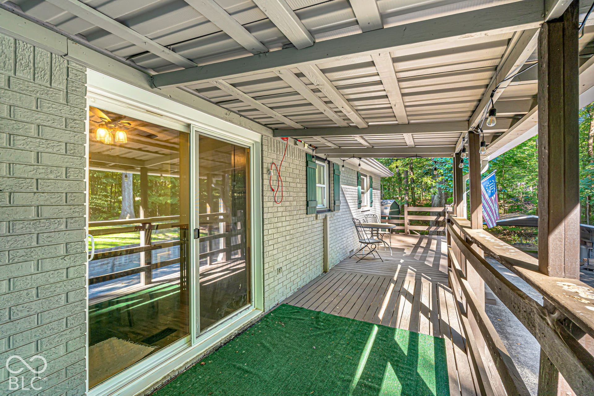 Covered deck with a metal roof and wood railing, featuring a brick exterior and sliding glass door