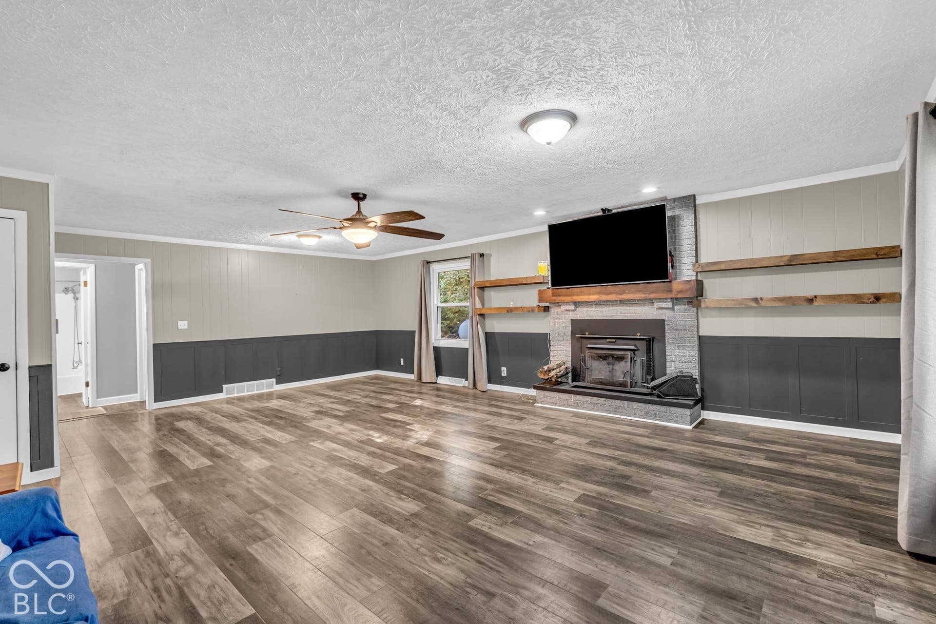 Wood-finish flooring throughout, board and batten wainscoting, ceiling fan with integrated lighting, brick fireplace with wood mantel, and built-in wood shelving
