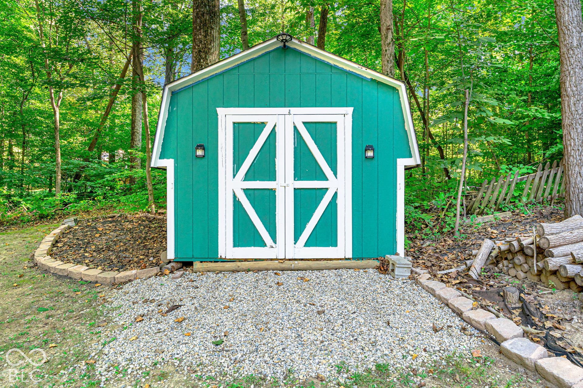 Gable-roof shed with teal siding, white double doors, and exterior wall sconces