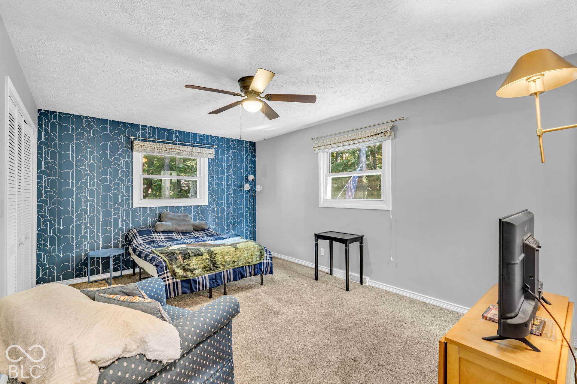 Carpeted flooring, ceiling fan, two windows with blinds, bi-fold closet doors, and patterned accent wall