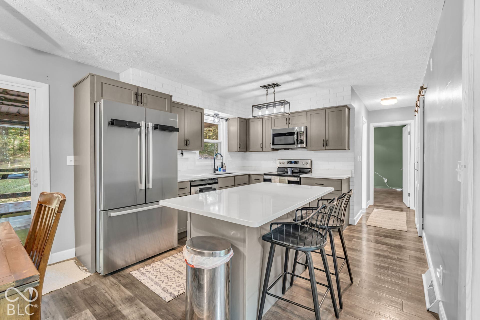 Kitchen featuring gray cabinetry, stainless steel appliances, a center island with a light-toned countertop, and wood-finish flooring