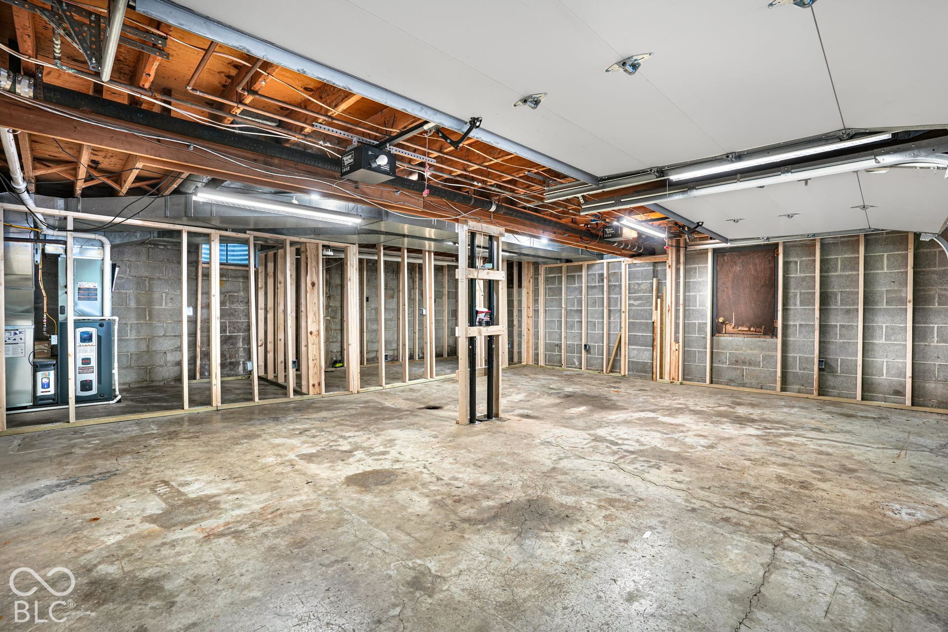 Unfinished basement featuring concrete block walls, concrete flooring, exposed wood ceiling joists, and exposed utility lines