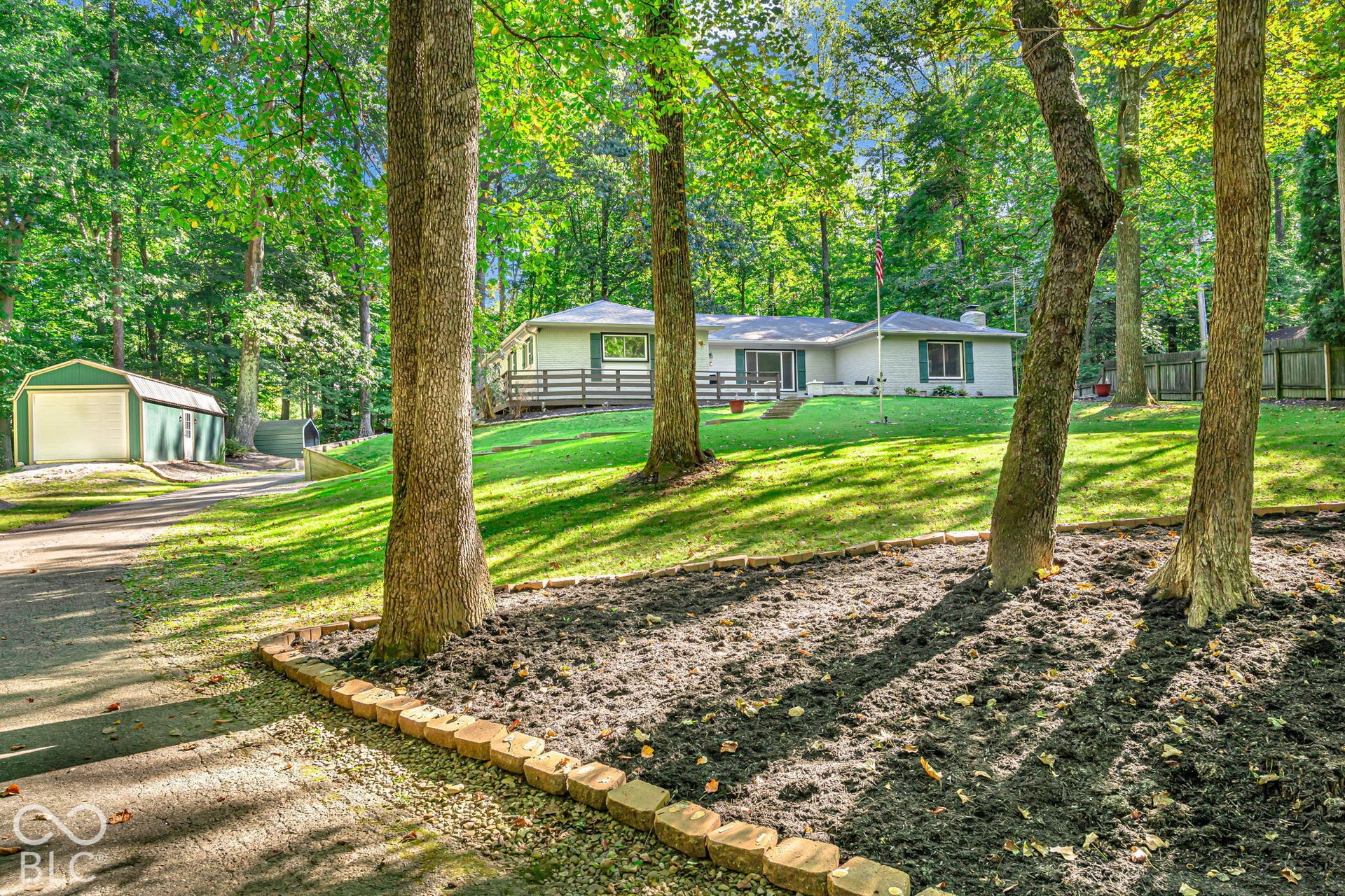 Ranch-style residence with a sprawling lawn, mature trees, and an expansive deck