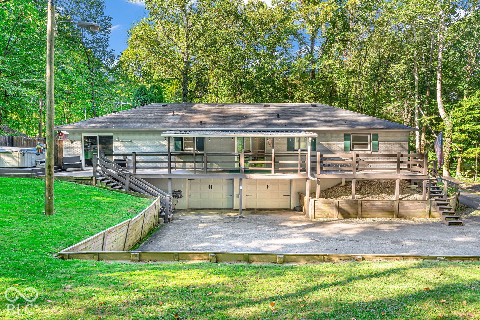 Expansive multi-level wood deck, dual garage bays, and a spa area surrounded by mature trees