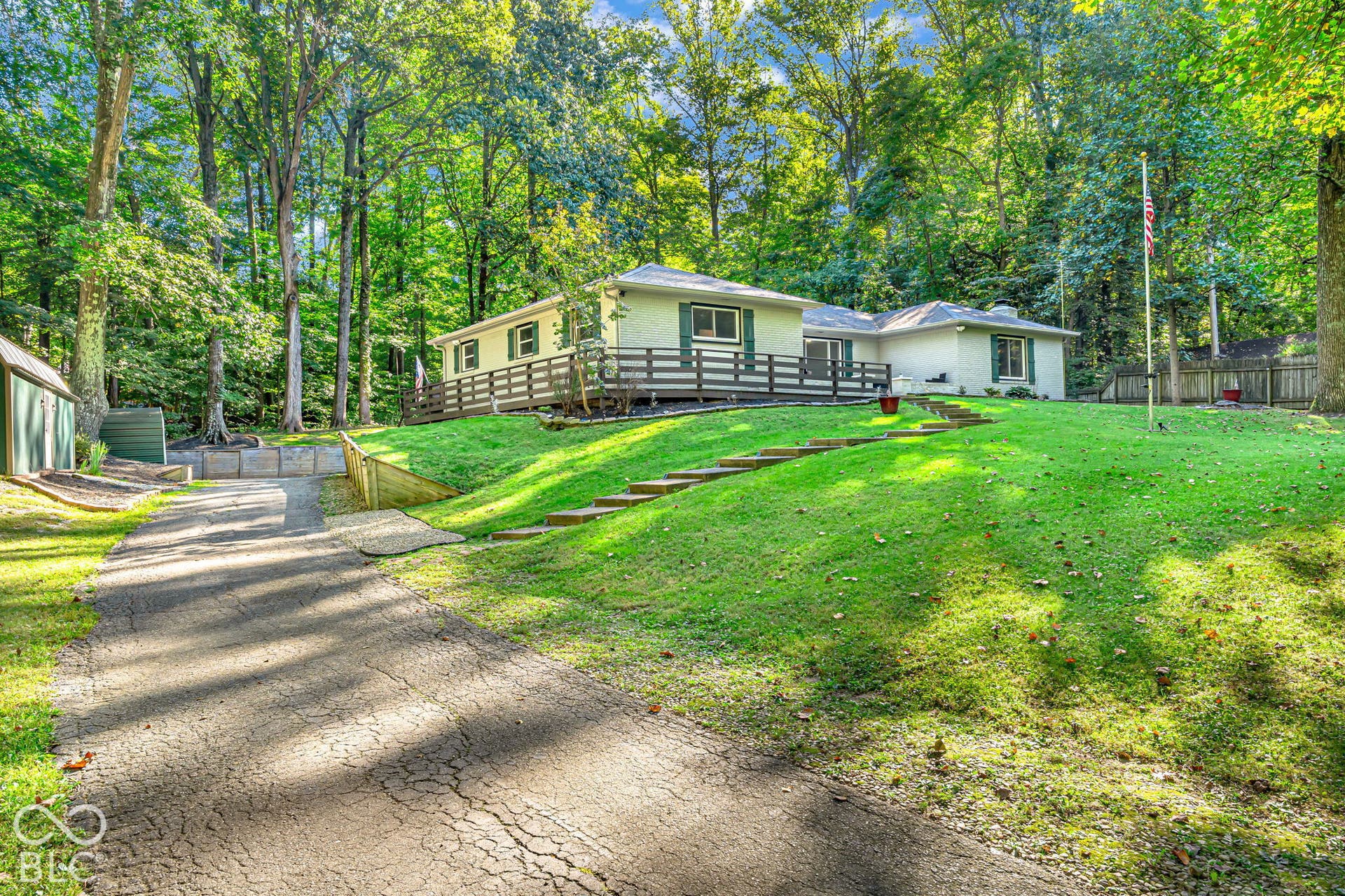 Ranch-style residence with a light-colored exterior and dark green shutters, surrounded by mature trees
