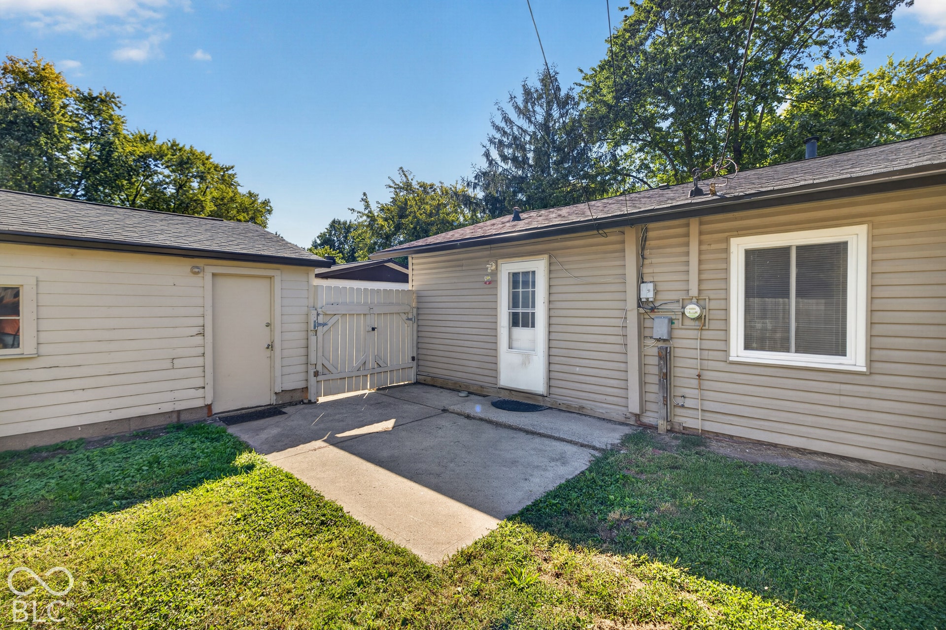 3241 Winton Avenue, Indianapolis, IN 46224 Concrete patio area with a white wooden gate, bordered by a detached structure with siding and a main structure with siding