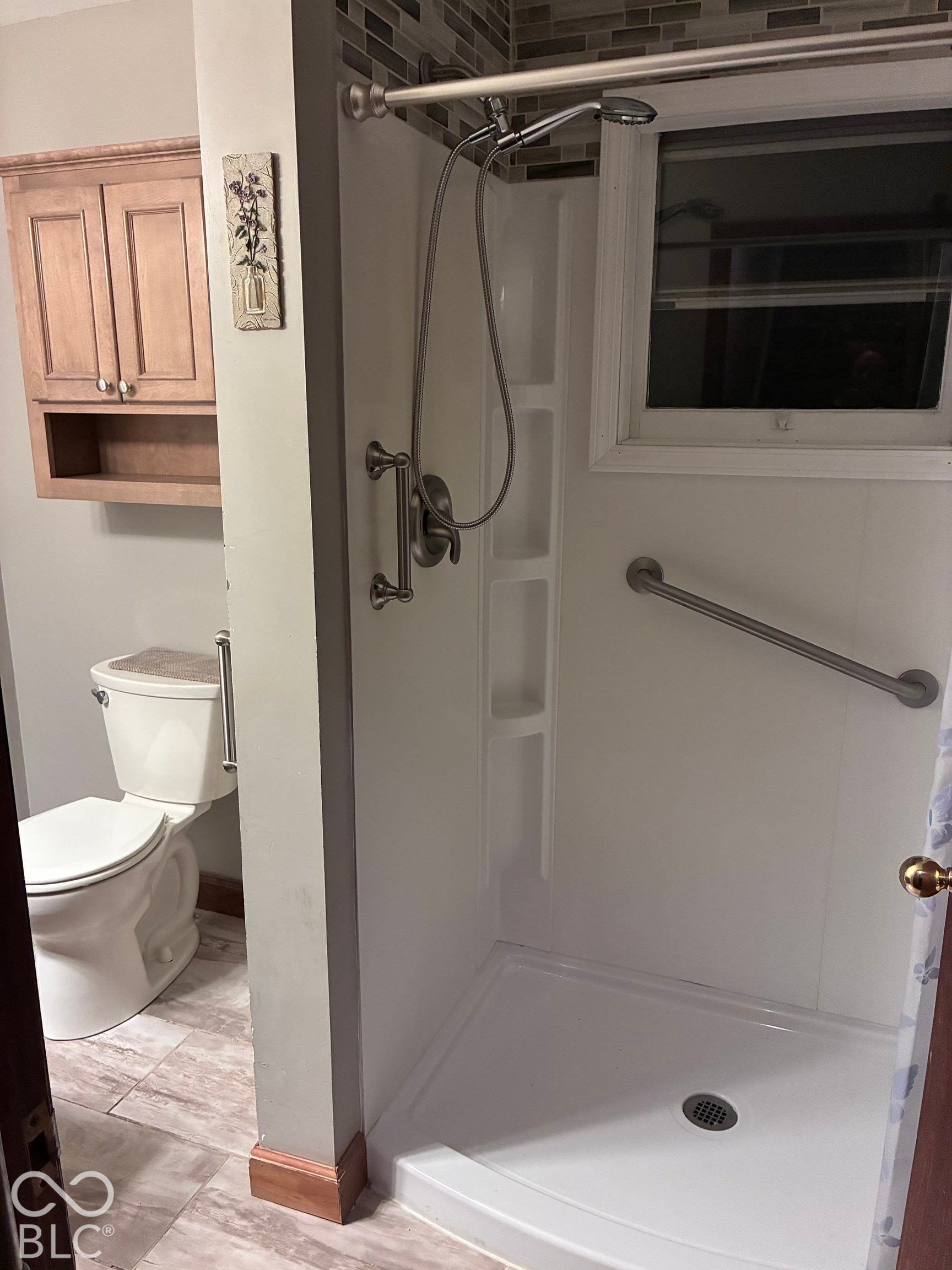 Walk-in shower with integrated shelving, matte silver fixtures, and a window
