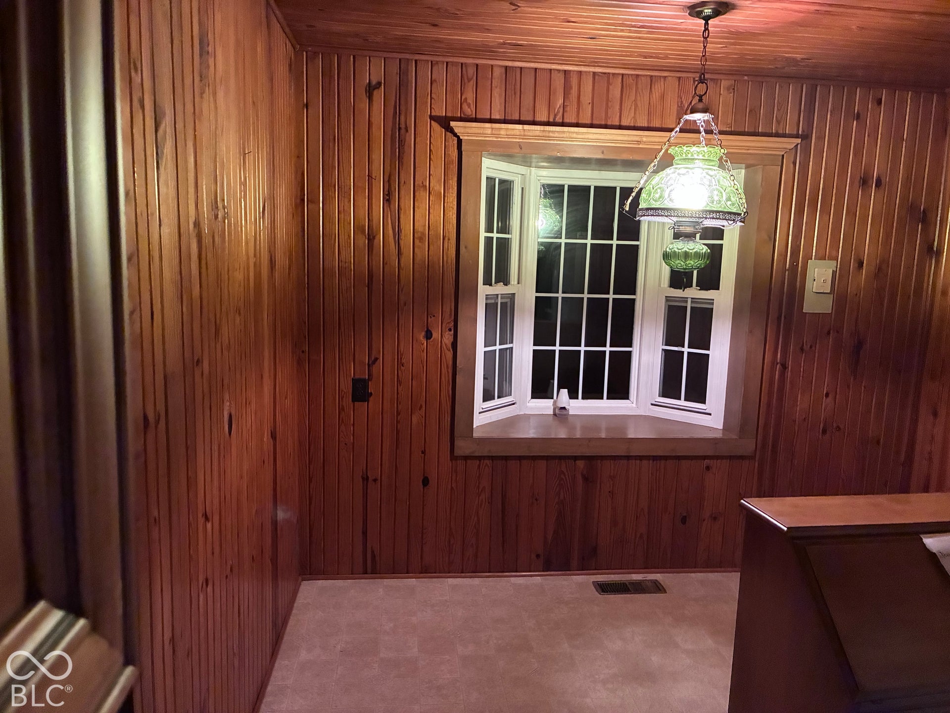 Wood-finish paneled walls and ceiling, bay window with white trim, and a decorative hanging light fixture