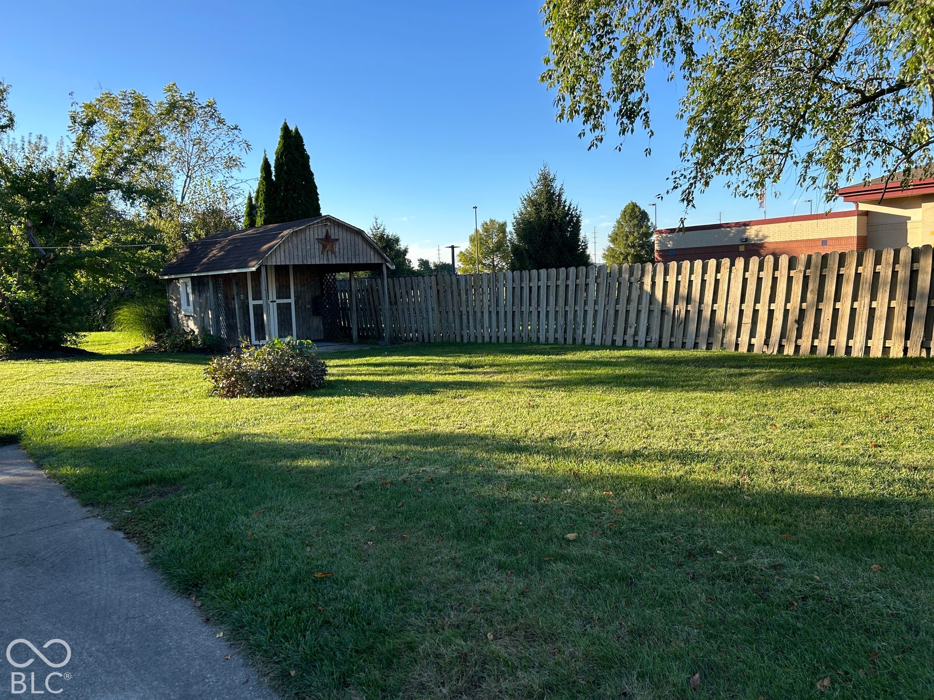 Expansive lawn featuring a wood privacy fence, a detached wood-sided shed with a gambrel roof, and mature trees
