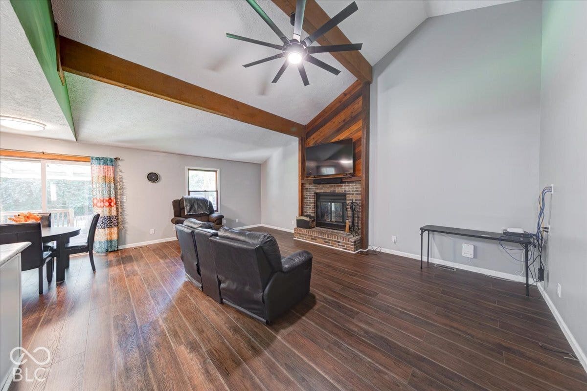Vaulted ceilings with exposed wood beams, LPV flooring, brick fireplace with wood surround, and sliding glass door
