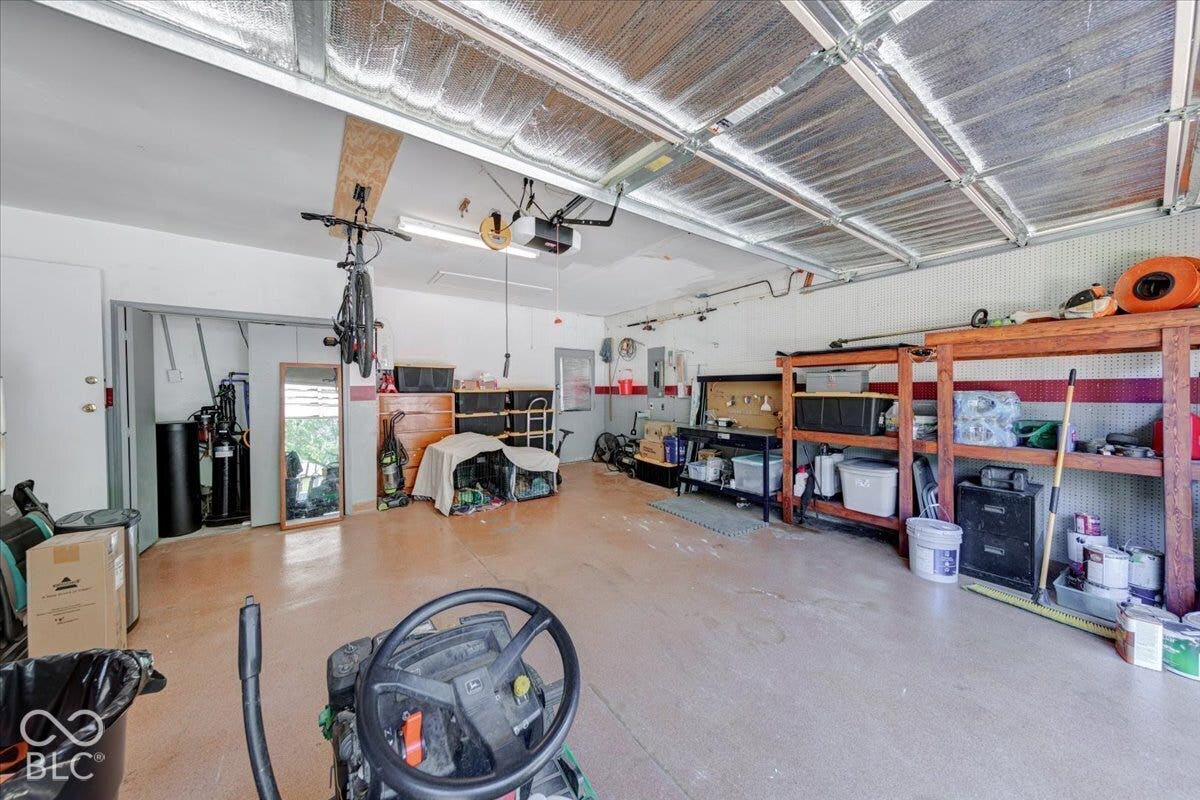 Spacious garage workshop featuring polished concrete flooring, exposed beam ceiling with integrated track lighting, and extensive built-in orange shelving and storage cabinetry along the perimeter