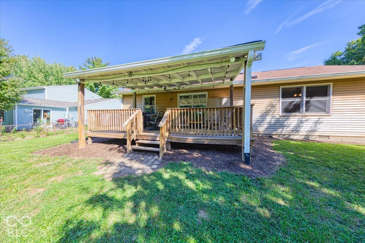 Covered wooden deck with railing, stairs, and mulch surrounding.