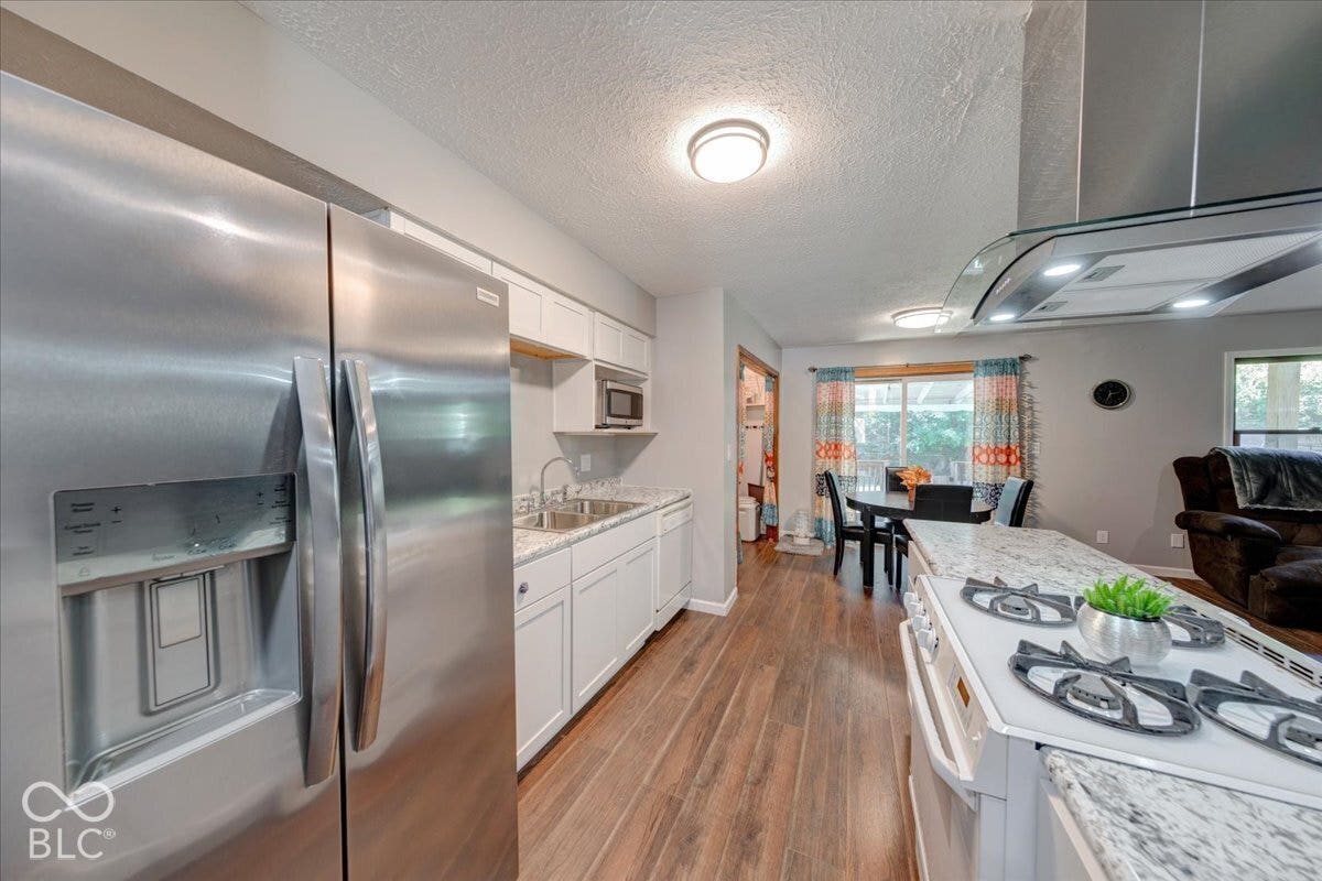 Modern kitchen with white cabinetry, laminate countertops, LVP waterproof flooring, appliance suite and range hood.