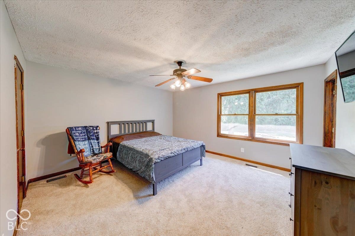 Spacious bedroom with new carpeting, wood-trimmed windows facing back yard,ceiling fan with integrated lighting, and wood-finish door frames throughout