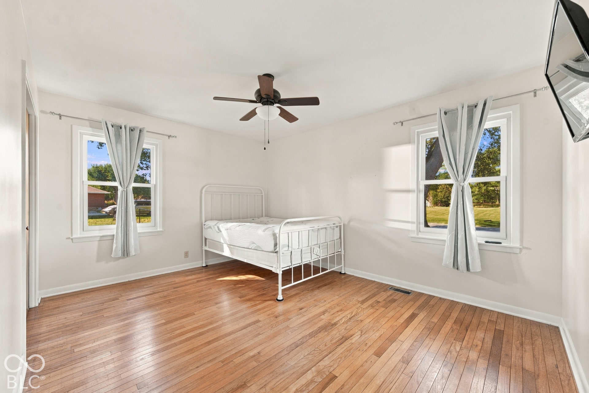 Hardwood flooring throughout, two double-hung windows, and a ceiling fan with integrated lighting