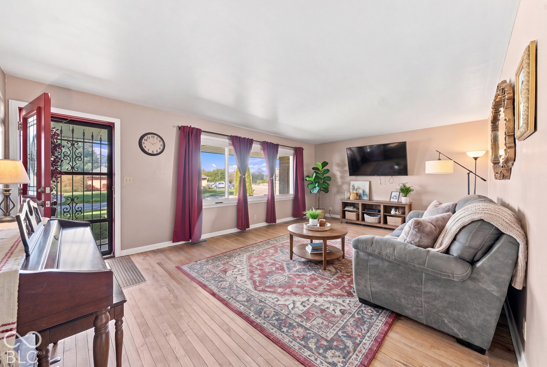 Virtually Altered - Wood-finish flooring throughout, light-toned walls, and an entryway with a red-framed door