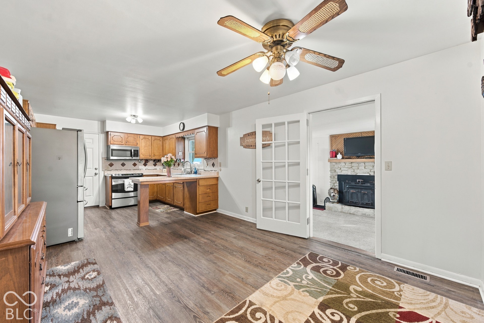 Open-concept living area featuring wood-finish flooring, a kitchen with wood cabinetry and stainless steel appliances, and a ceiling fan