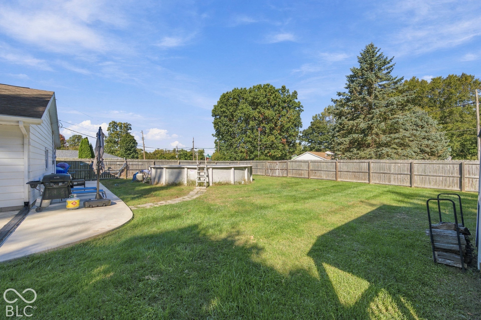 Expansive backyard featuring a privacy fence, concrete patio, above-ground pool, and mature trees