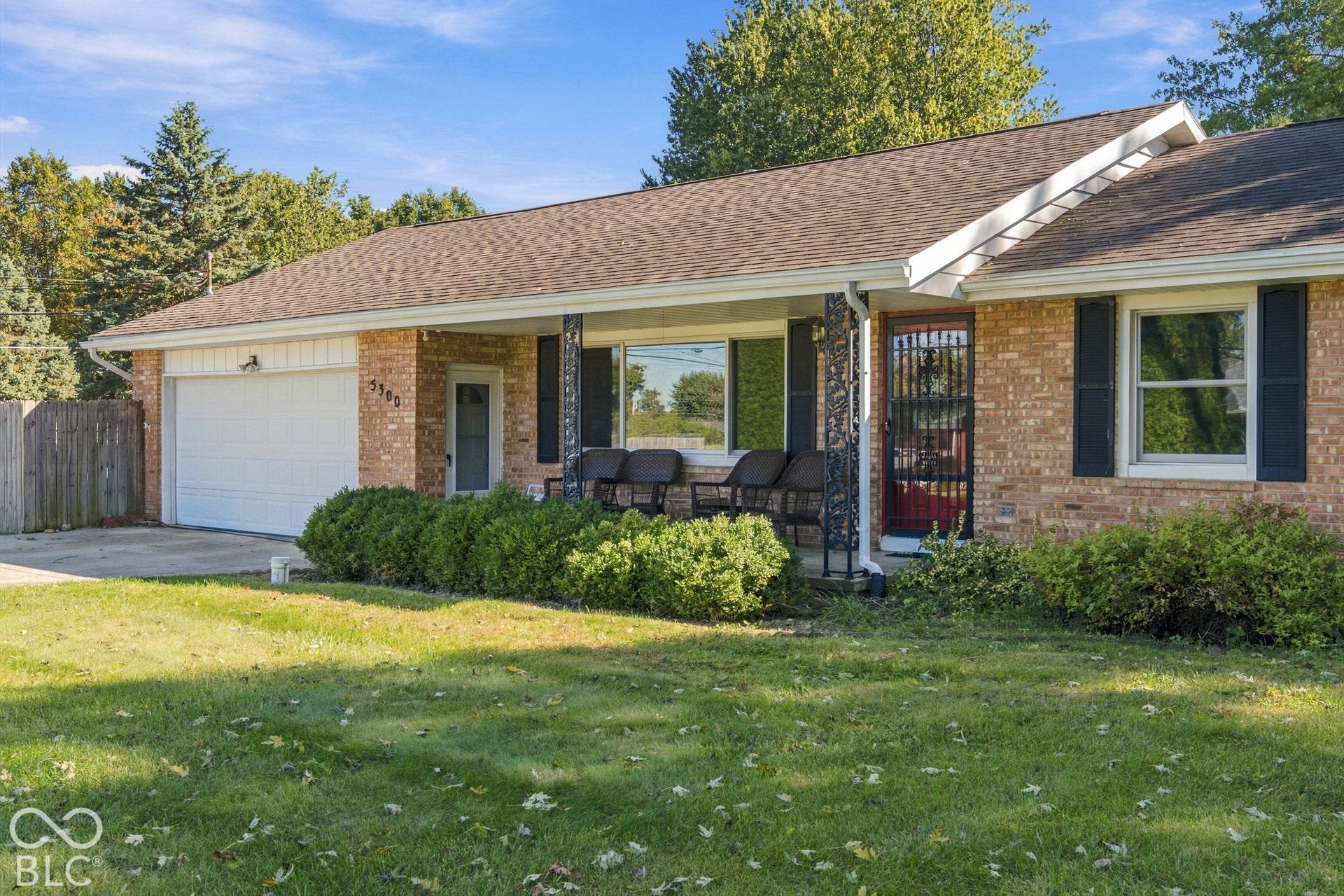 Welcoming brick ranch home featuring a covered front porch with black columns, large picture windows, and an attached two-car garage