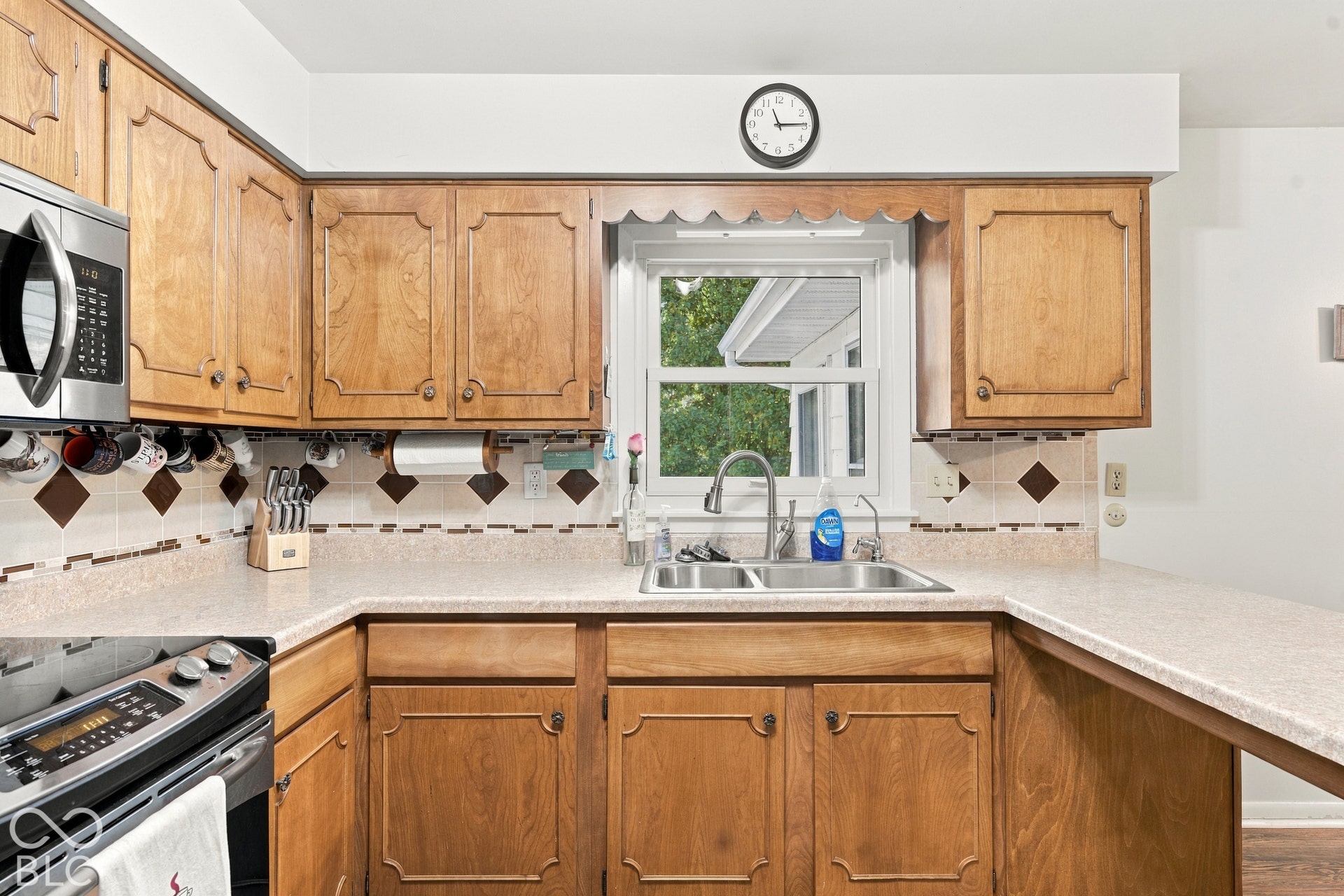 Wood cabinetry, stainless steel microwave, dual basin sink, window, and backsplash with decorative accents