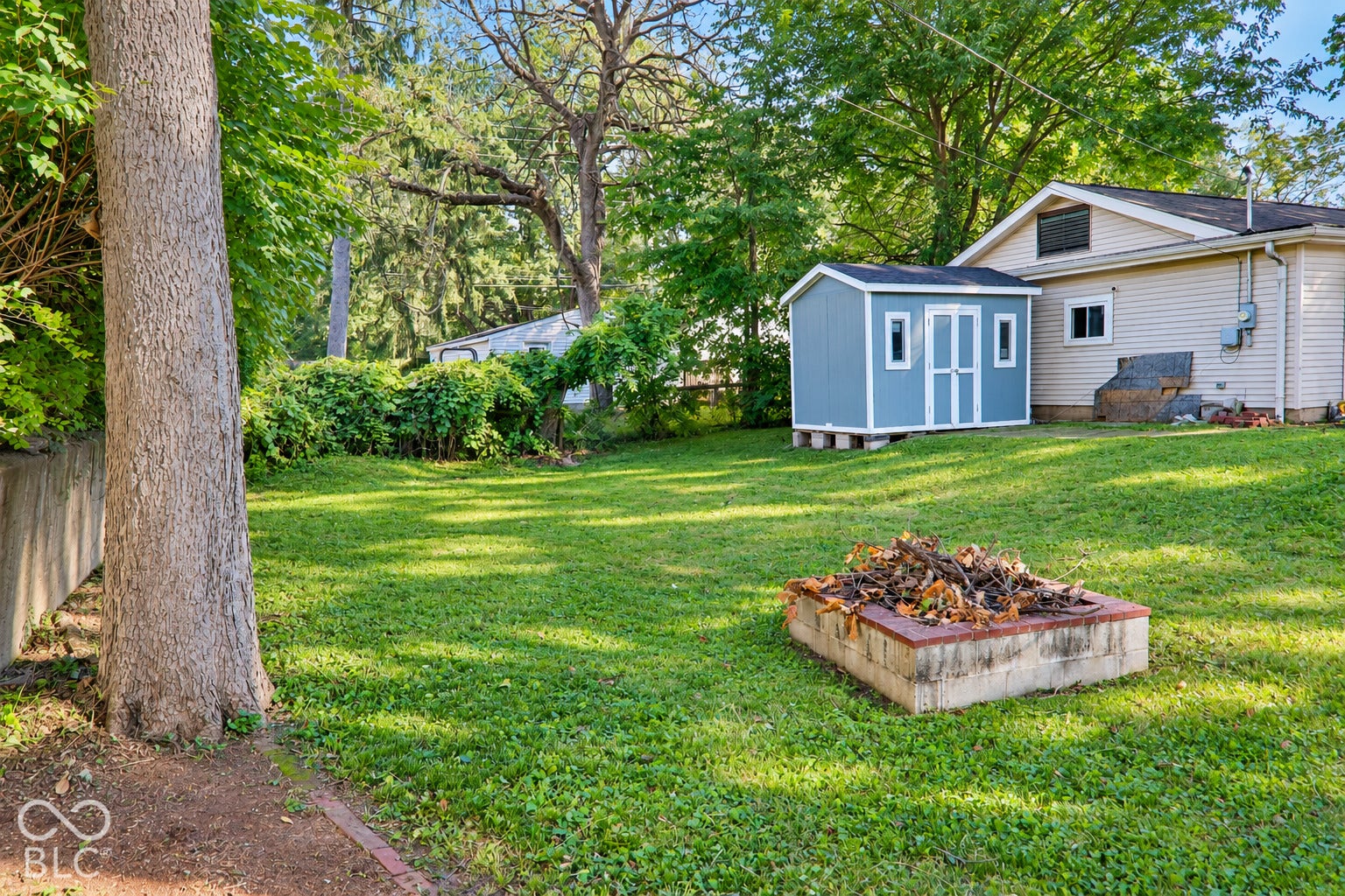 3566 Watson Road, Indianapolis, IN 46205 Expansive grassy yard featuring mature trees, a detached storage shed, and a built-in fire pit
