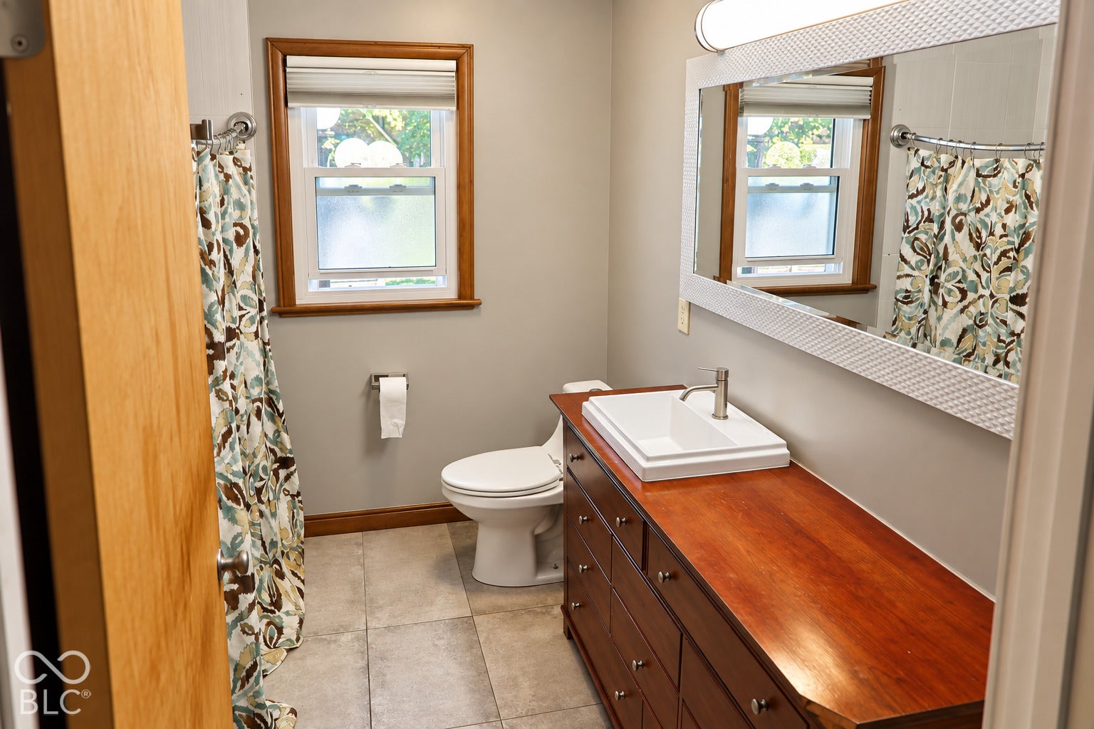 3566 Watson Road, Indianapolis, IN 46205 Modern bathroom featuring a wood-finish vanity with an integrated vessel sink, a full-width mirror with a decorative frame, and tiled flooring