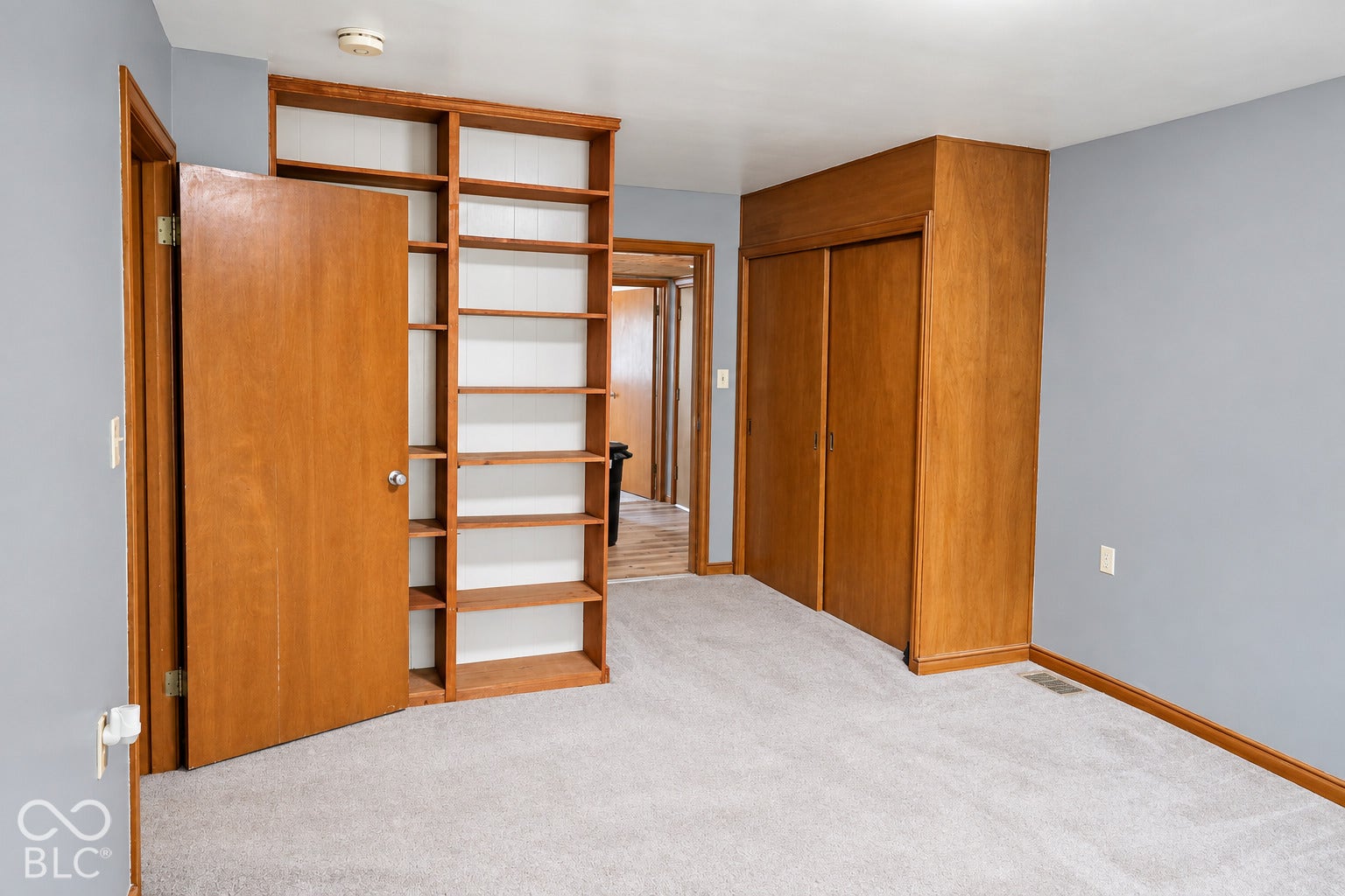 3566 Watson Road, Indianapolis, IN 46205 Built-in wooden shelving, gray painted walls, light gray carpet flooring, and wooden bi-fold closet doors