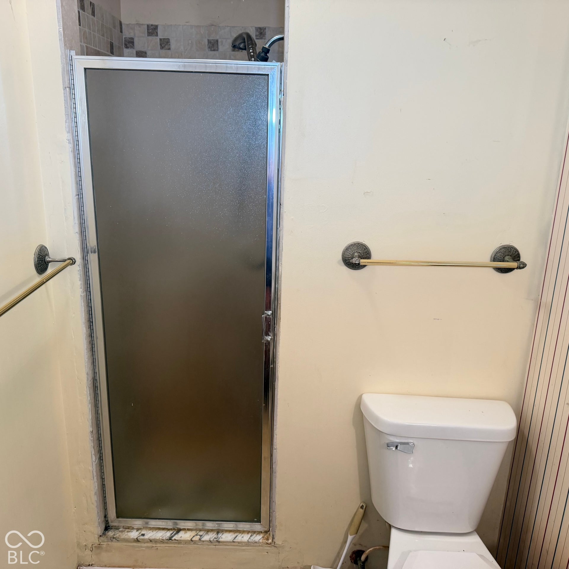 Frosted glass shower enclosure with chrome framing, tiled shower surround, and a white toilet