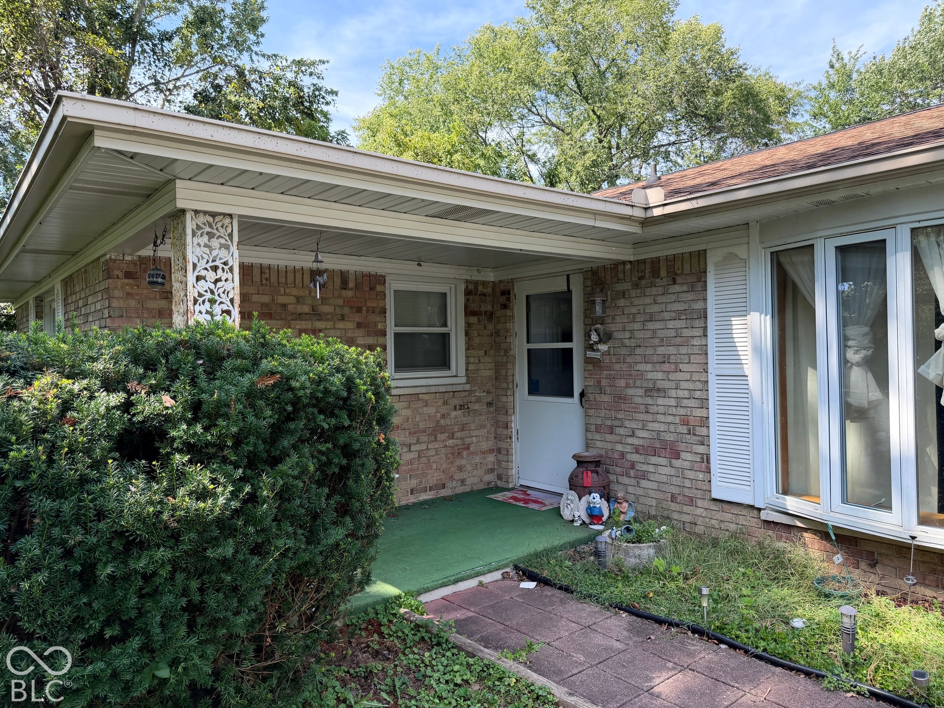 Brick exterior, covered entry, front porch with decorative column, mature shrubbery, front walkway