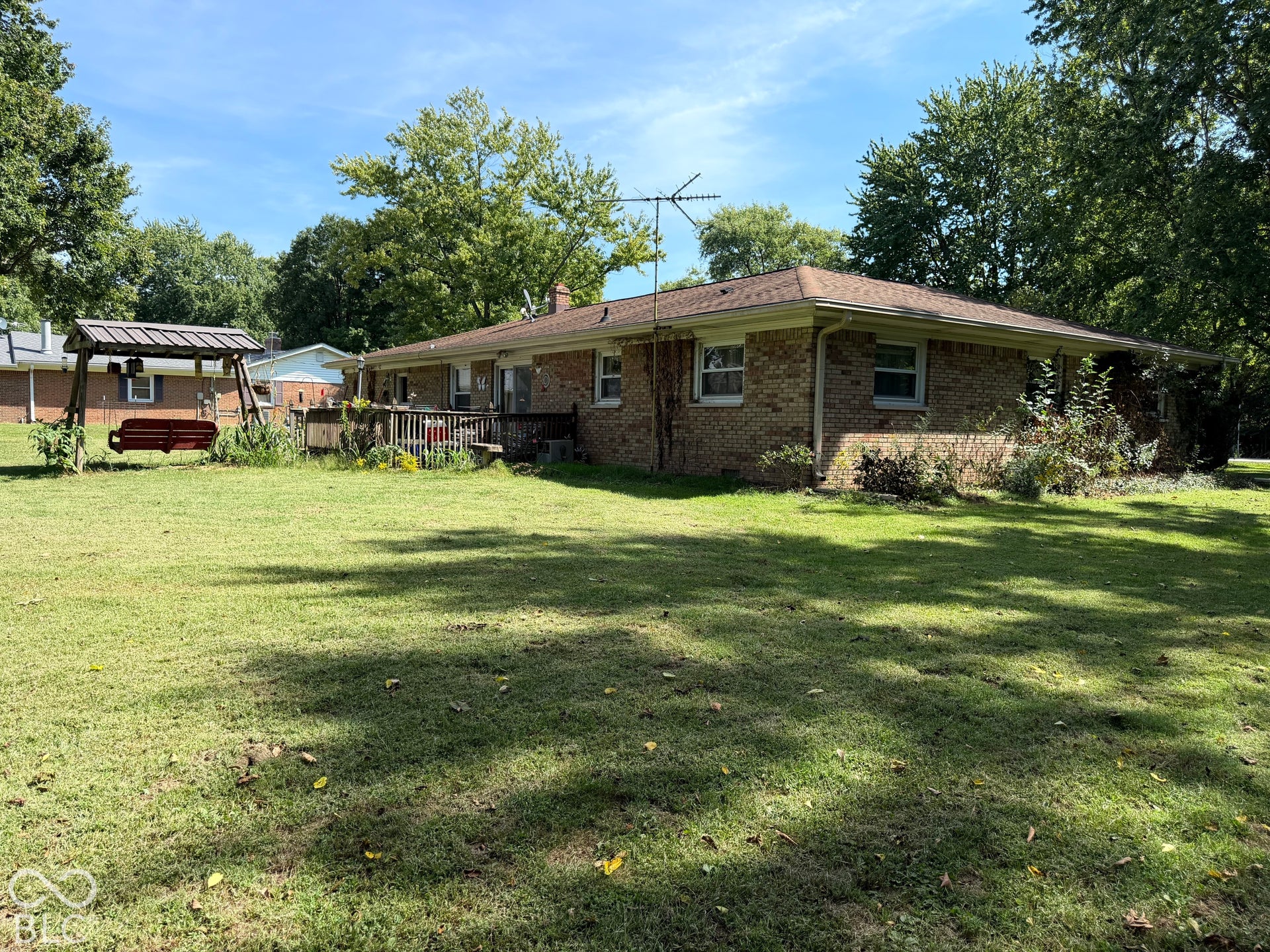 Brick exterior with a brown shingle roof, accompanied by a wooden deck and a lush lawn