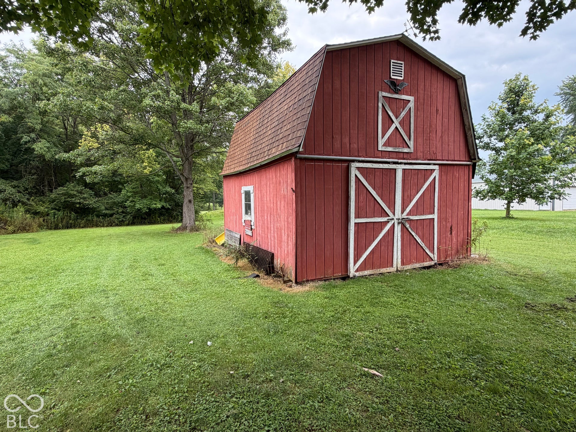 Red barn structure with a gambrel roof, white cross-buck double doors, and a decorative gable vent