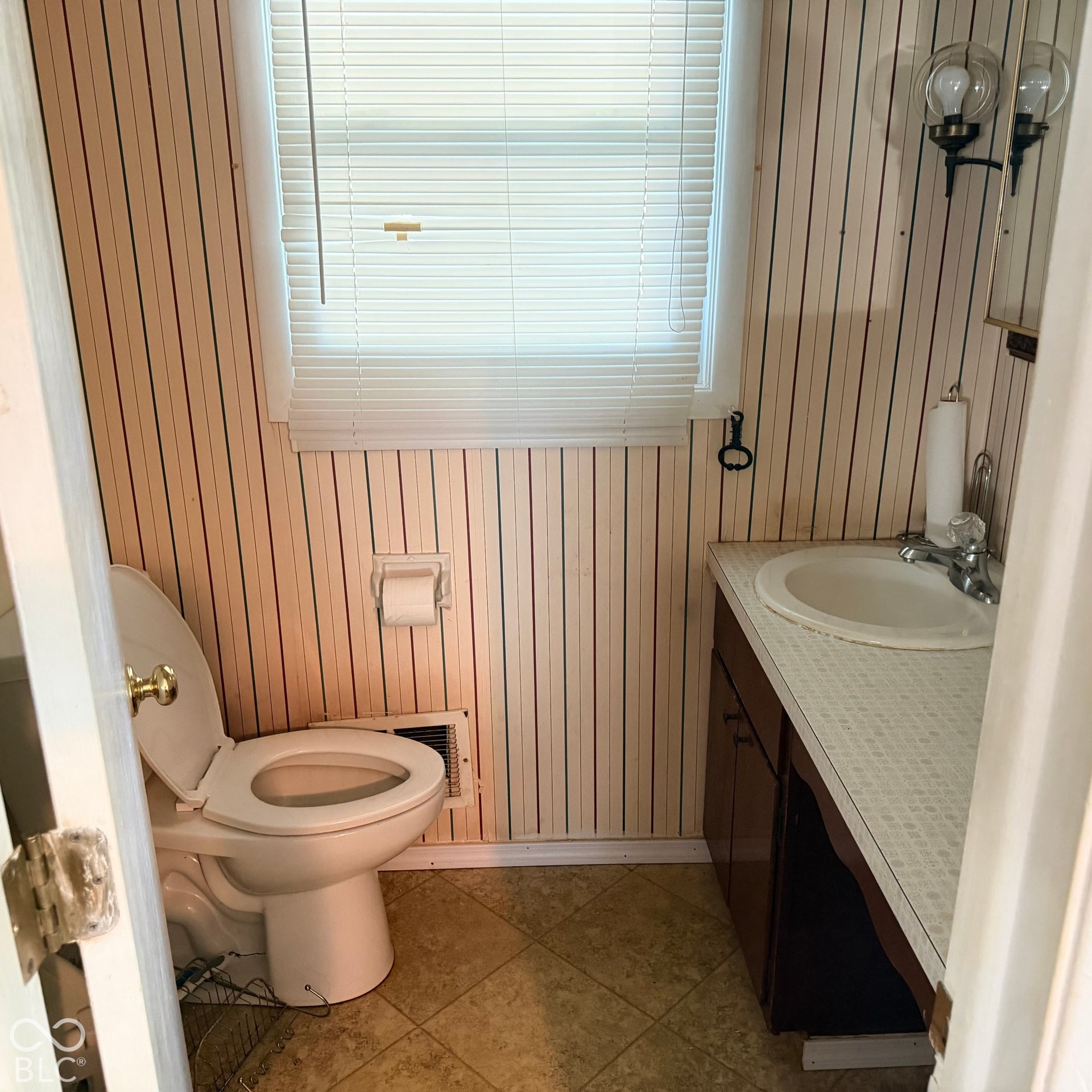Vanity with an integrated sink, wall-mounted light fixture, and window with blinds