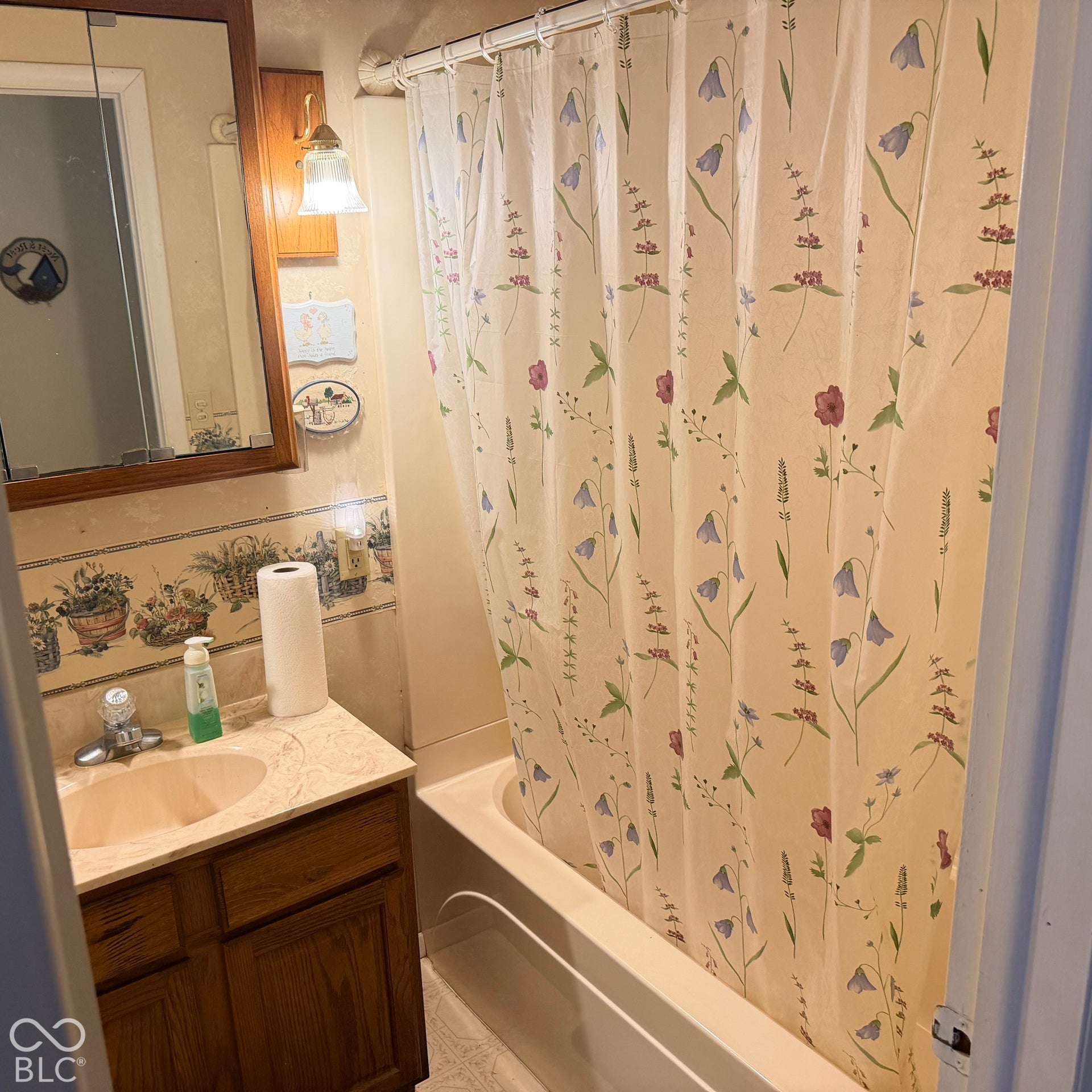 Bathtub with shower, wood-finish vanity with countertop and integrated sink, wall-mounted medicine cabinet with mirror, and wall-mounted light fixture