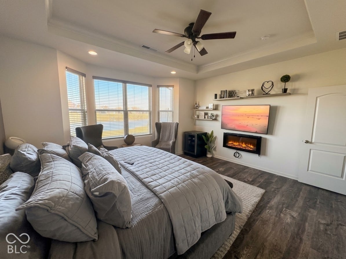 Tray ceiling with recessed lighting, wood-finish flooring, ceiling fan light fixture, bay windows, and a wall-mounted electric fireplace