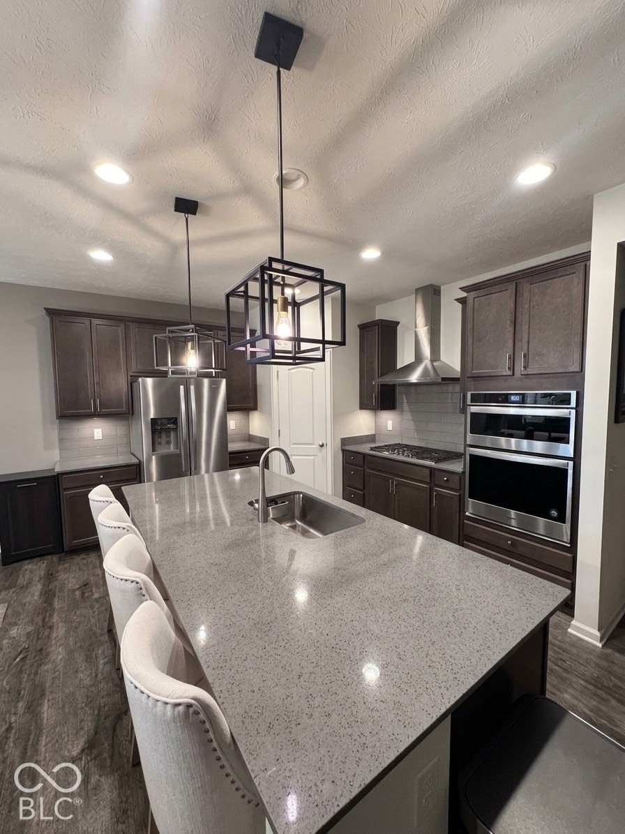Kitchen featuring a large central island with an integrated sink, dark wood-finish cabinetry, stainless steel appliances, and recessed lighting