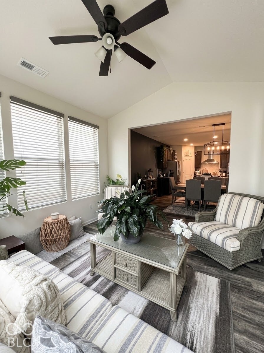 Vaulted ceiling with a ceiling fan light fixture, wood-finish flooring, and multiple windows