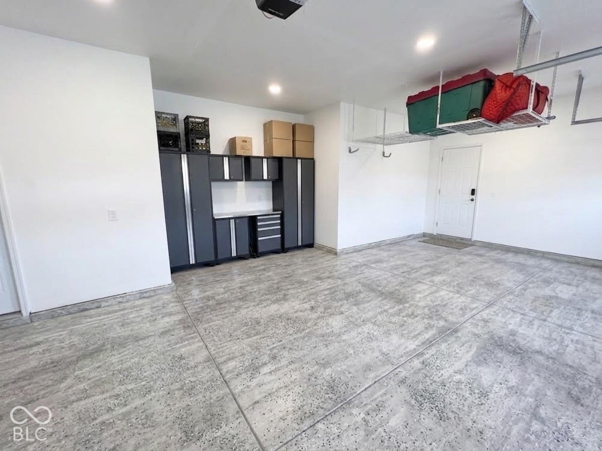 Concrete flooring with textured finish, built-in cabinetry, overhead storage racks, recessed lighting, and a solid entry door