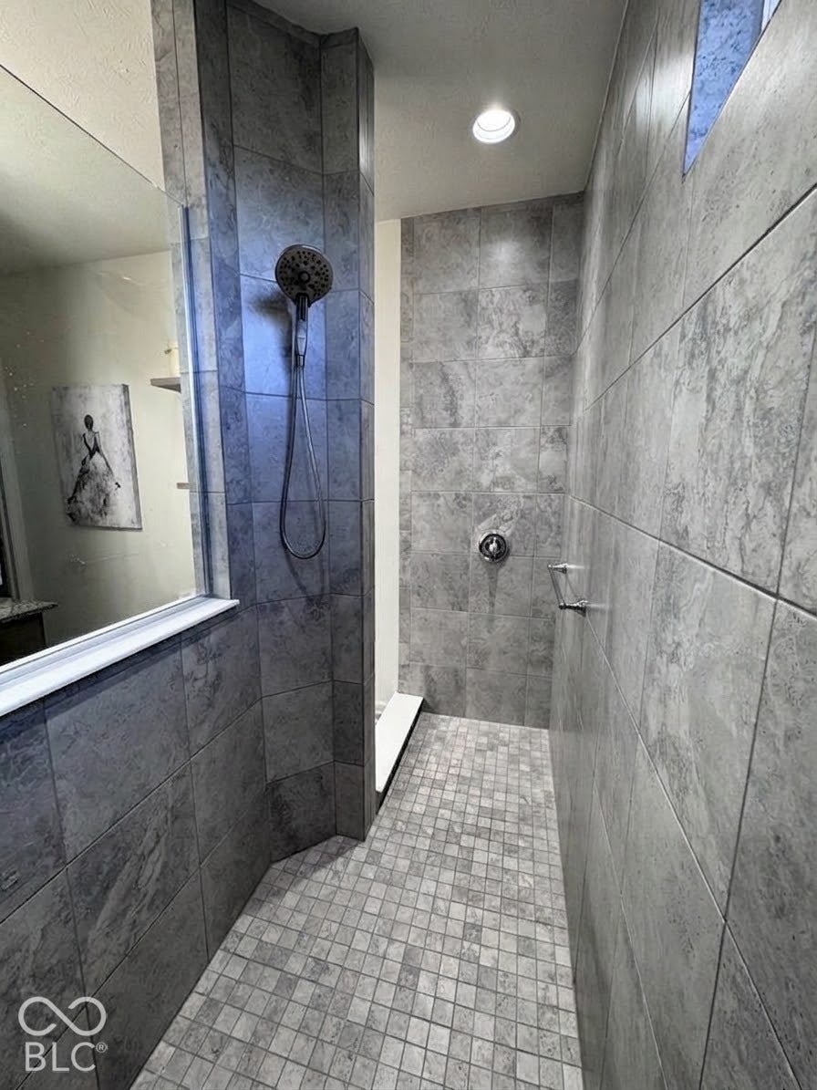 Tiled shower with a built-in bench, recessed lighting, and a handheld shower fixture