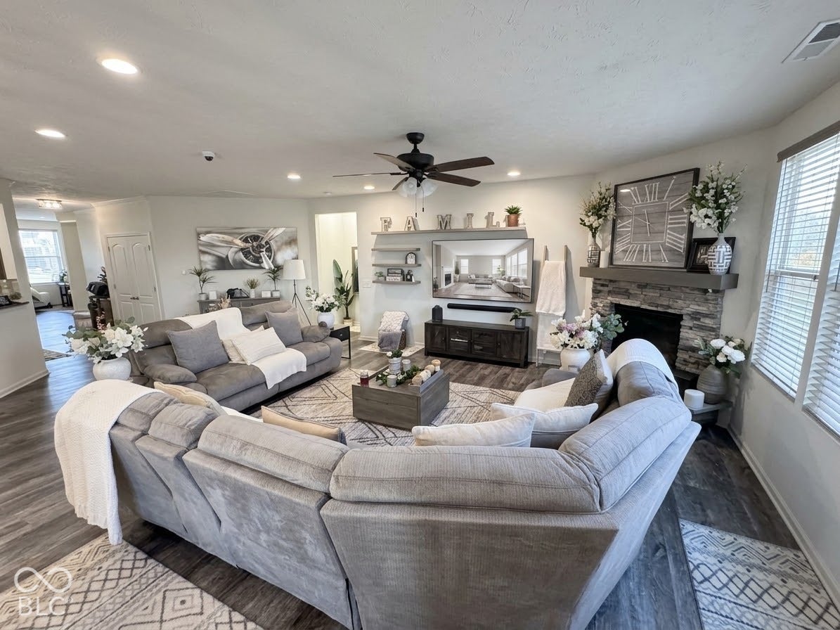Spacious living area featuring wood-finish flooring, recessed lighting, and a stone-faced fireplace with a mantel