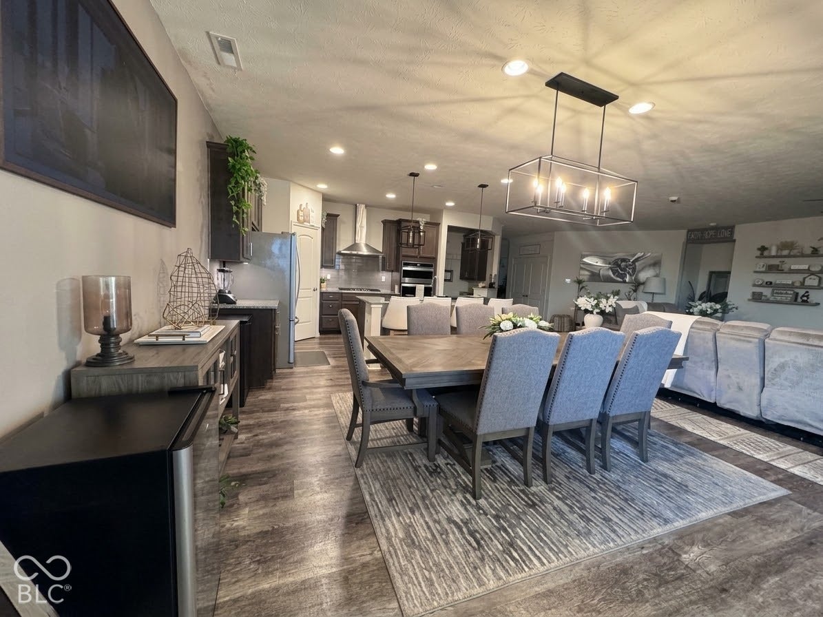 Open-concept living area featuring wood-finish flooring, recessed lighting, and a linear chandelier